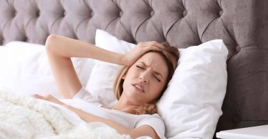 Young woman suffering from headache while lying in bed. Sleeping problems